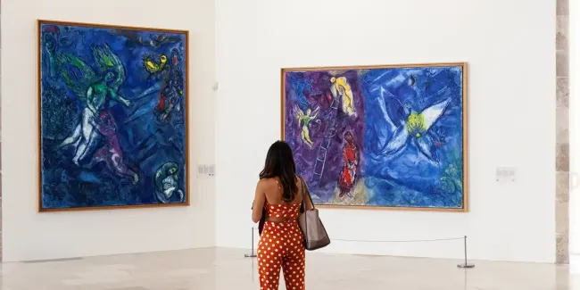 Visiteuse dans la salle du Message Biblique, devant les oeuvres de Marc Chagall, La Lutte de Jacob et l’Ange (1960-1966, huile sur toile, 251 x 205 cm) et Le Songe de Jacob (1960-1966, huile sur toile, 195 x 278 cm). Nice, musée national Marc Chagall © Musées nationaux du XXe siècle des Alpes-Maritimes/ Gilles Erhentrant / Adagp, 2026